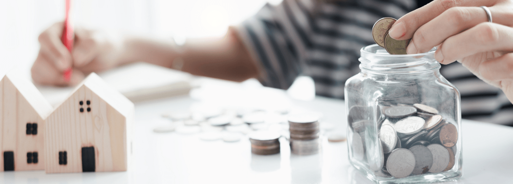 Woman at a desk with jar of money and wooden house models to demonstrate the cost of buying a house